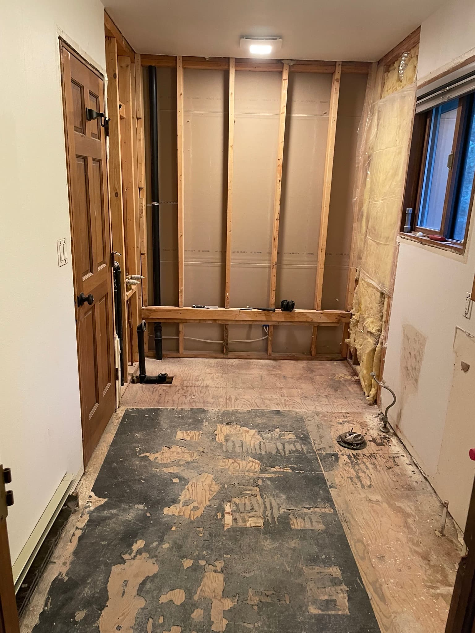 Looking into the bathroom from the doorway during demo: walls stripped, old vinyl pulled, exposed adhesive on the subfloor.
