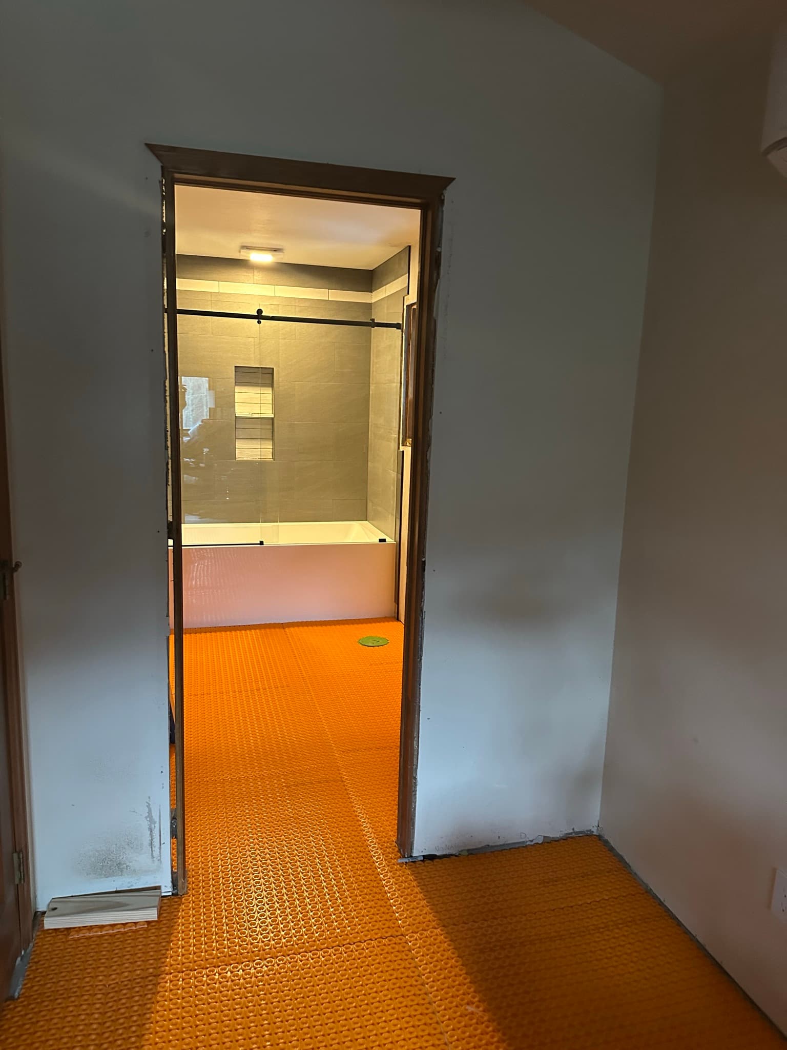 Schluter Ditra-Heat uncoupling membrane installed on the subfloor: orange waffle-textured sheet covering the bathroom floor, viewed from the hallway through the doorway.