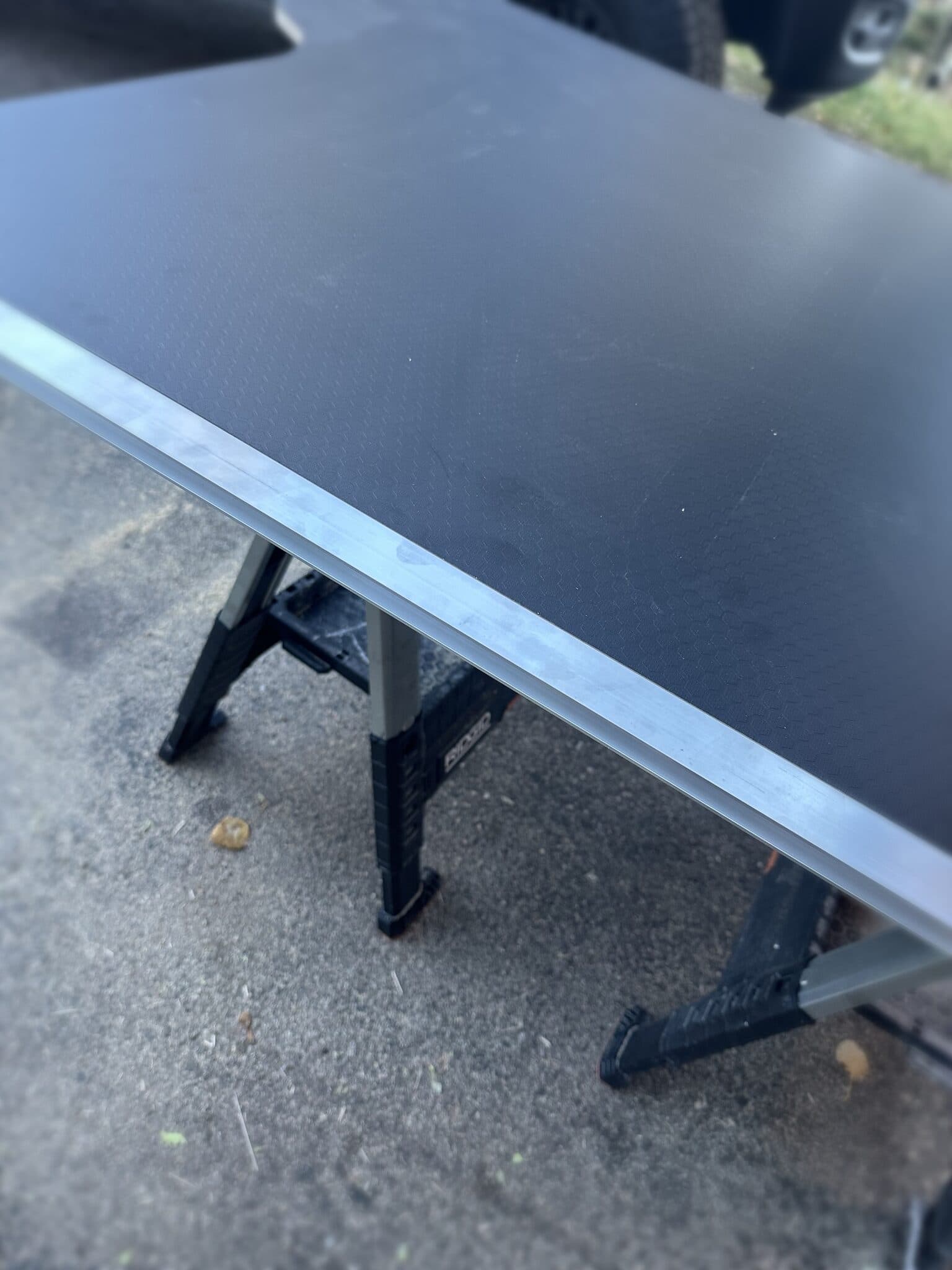 Close-up of the deck panel's edge on sawhorses, showing a brushed aluminum trim strip along the laminated plywood edge.