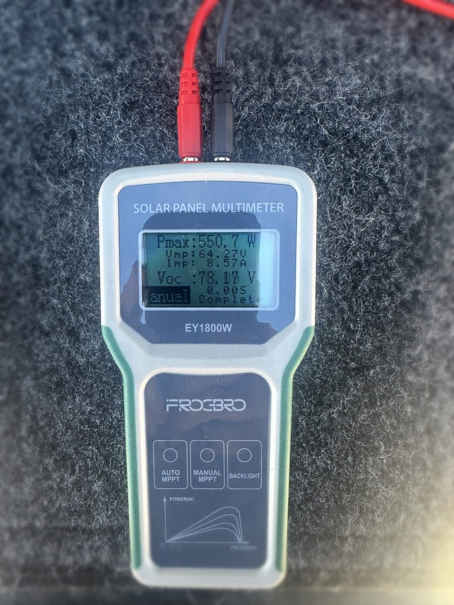 Handheld solar panel multimeter clipped to a panel showing Pmax 550.7 watts, Vmp 64.27 volts, Imp 8.57 amps, and Voc 78.17 volts.
