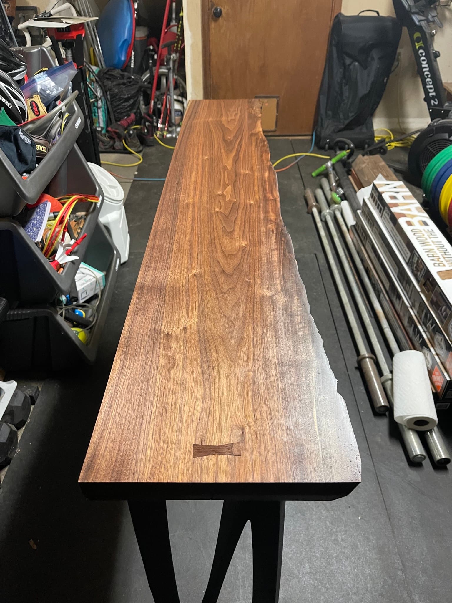 Finished walnut slab top sitting on saw horses in the shop before install, two bowtie inlays visible along the length, live edge curving along one side.