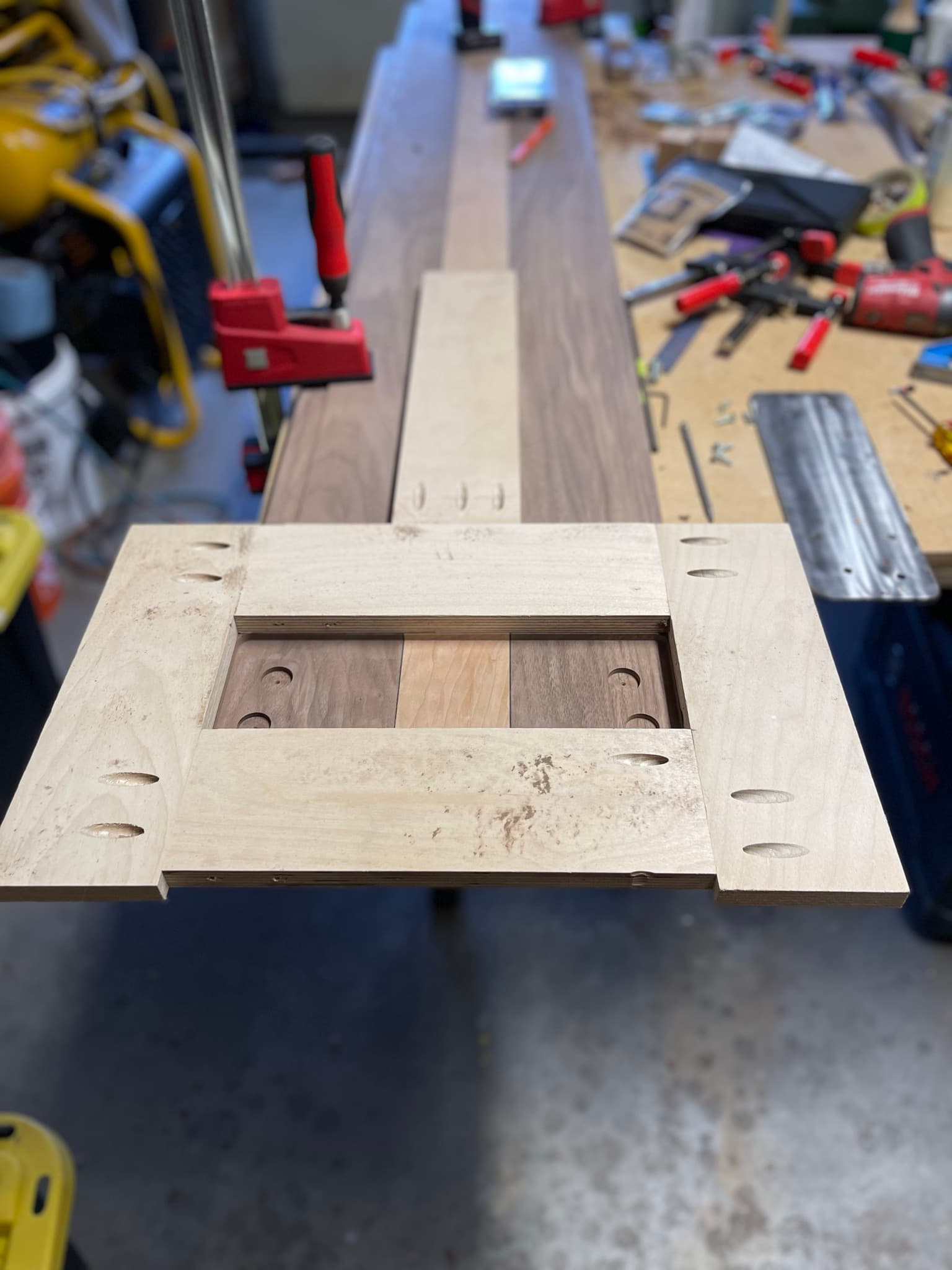 The maple-walnut sandwich top under red Bessey clamps during glue-up in the shop, a leg mounting block sitting at the foreground.